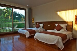 A hotel room with two beds, a large sliding glass door leading to a balcony, and a wooden floor.