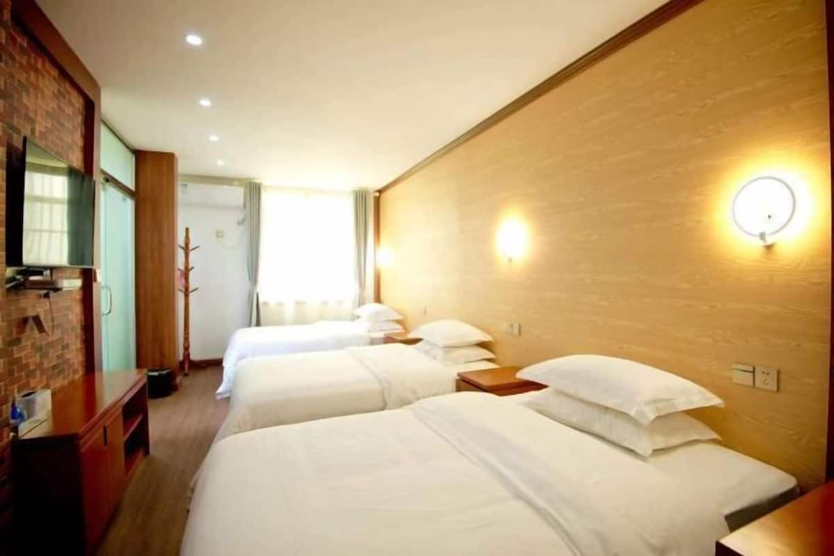 Ett hotellrum med tre enkelsängar, en TV, en väggpanel i trä och en lampa.