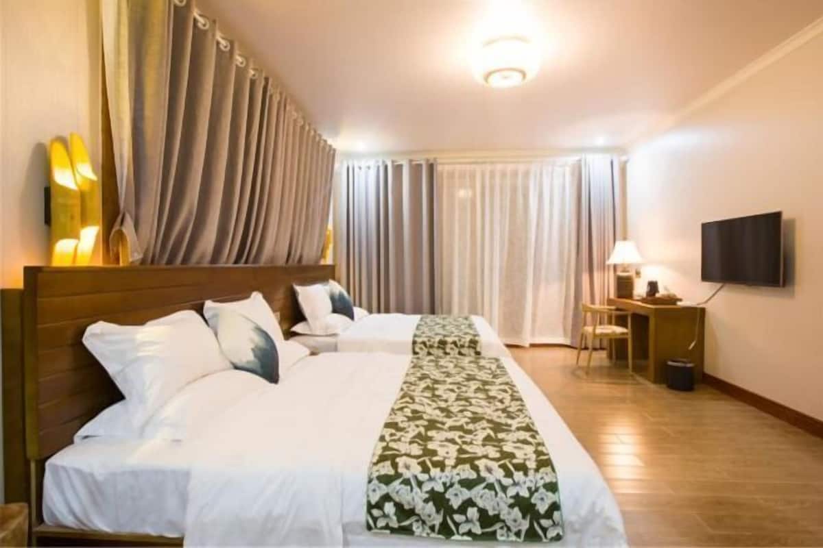 Ett hotellrum med en stor säng, ett skrivbord, en stol, en tv och gardiner.