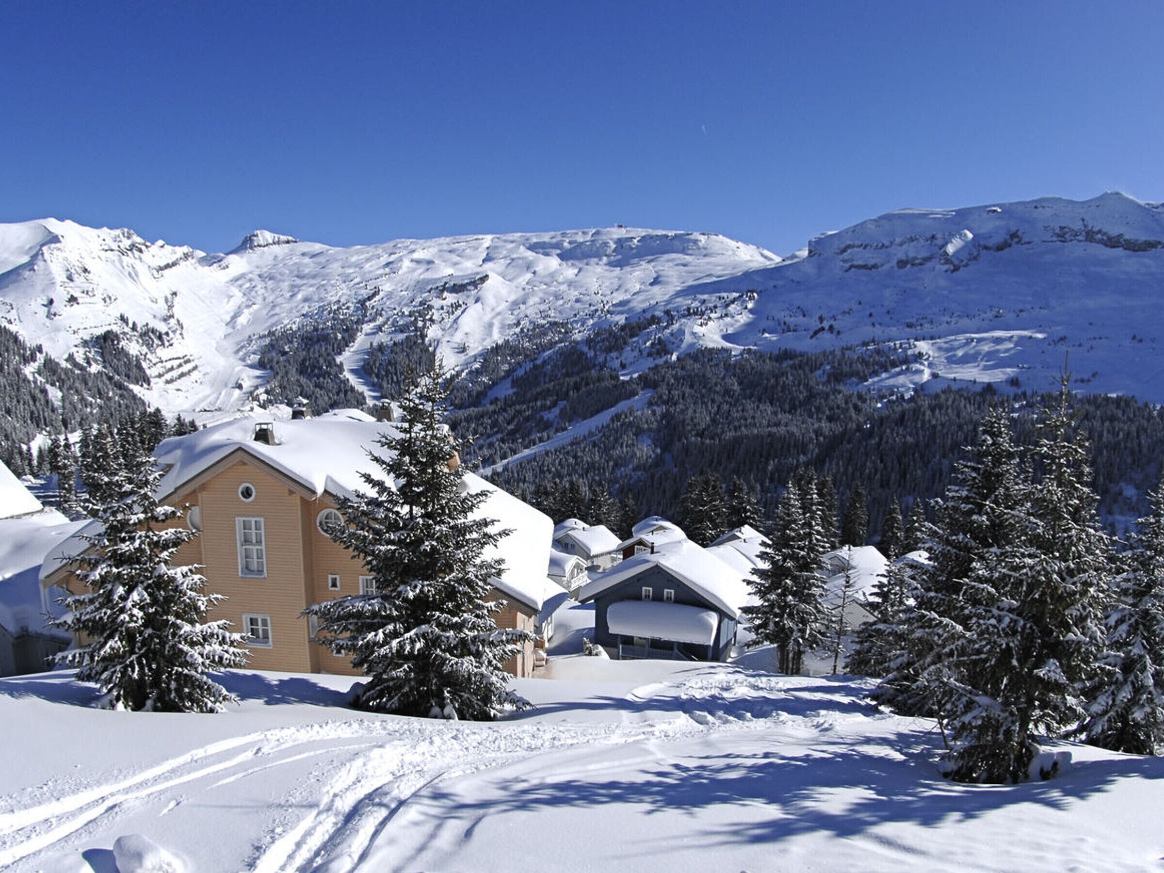 Un paysage montagneux enneigé avec un bâtiment de style chalet, doté d’une grande fenêtre et d’une cheminée.