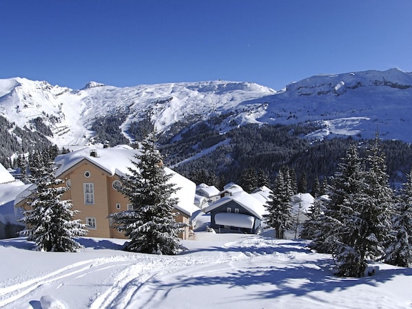 A snow-covered mountain landscape with a chalet-style building featuring a large window and a chimney.