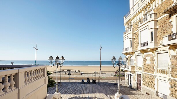 Eine Küstenpromenade mit Blick auf den Strand, ein Fußweg und ein Gebäude mit Balkonen.