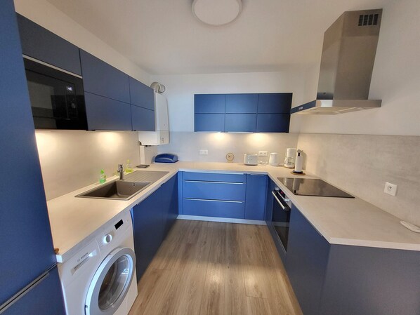 A compact kitchen with blue cabinets, a built-in washing machine, and modern appliances. - Renovated T3 apartment sea view with garage and WIFI (Les Sables-d'Olonne)