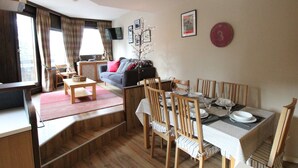 Un coin repas avec une table dressée pour quatre personnes, des chaises en bois et un canapé en arrière-plan.