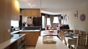 Une cuisine compacte avec des meubles en bois, un coin repas avec une table pour quatre personnes et un espace de vie comprenant un canapé et un téléviseur.
