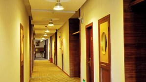 Un pasillo de hotel con varias puertas, una alfombra estampada e iluminación colgante.