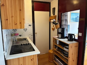 A compact kitchen with a gas stove, sink, and wooden shelves with cookware.