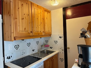 A kitchen with wooden cabinets, a stove, a sink, and a coffee maker. - Cozy Apartment Near the Slopes - Sleeps 6 - 2 Bedrooms (La Plagne)