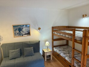 Ein Zimmer mit einem Etagenbett, einer Schlafcouch, einem kleinen Nachttisch, einer Lampe und einem gerahmten Bild an der Wand.