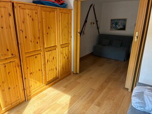 Una habitación con armarios de madera, un sofá gris y esquíes apoyados en la pared.
