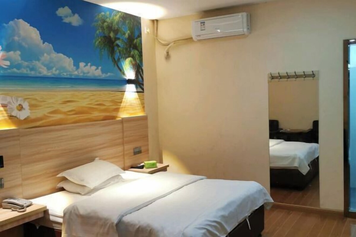 A hotel room with a beach mural, a single bed, a bedside table with a phone, and a wall-mounted air conditioner.