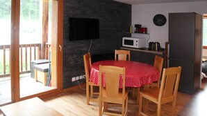 A cozy room with a wooden dining table, chairs, a flat-screen TV mounted on a dark brick wall, a microwave, and a refrigerator. - Renovated apartment for 8 with pool, jacuzzi and sauna in Les Orres (Les Orres)