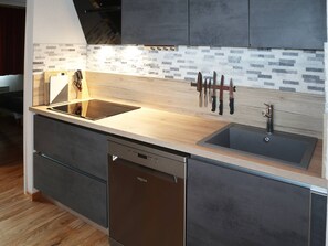 Een moderne keuken met een houten aanrecht, een inbouwvaatwasser en een spatwand met een baksteenmotief.