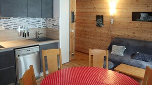 A compact kitchen with a dishwasher, a wooden dining table with a red polka dot tablecloth, and a sofa with a blue blanket. - Renovated apartment for 8 with pool, jacuzzi and sauna in Les Orres (Les Orres)