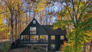 Eine dunkel gefärbte Holzhütte mit Balkon, umgeben von Bäumen im Herbstlaub.