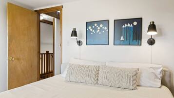 A bedroom with a bed, two wall-mounted lamps, and two framed artworks.
