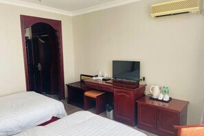 Habitación de hotel con dos camas, un escritorio con televisor, un armario y un mueble pequeño con artículos de aseo.
