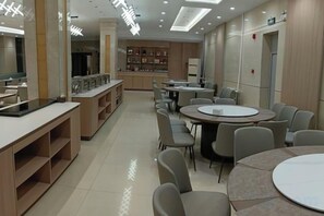 Un comedor moderno con mesas y sillas redondas, una barra con una vitrina y una zona de cocina al fondo.