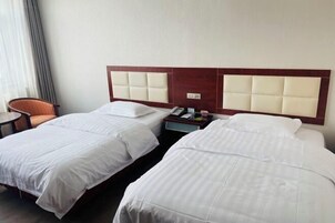 A hotel room with two beds, a wooden headboard, a bedside table with a lamp, and a chair.
