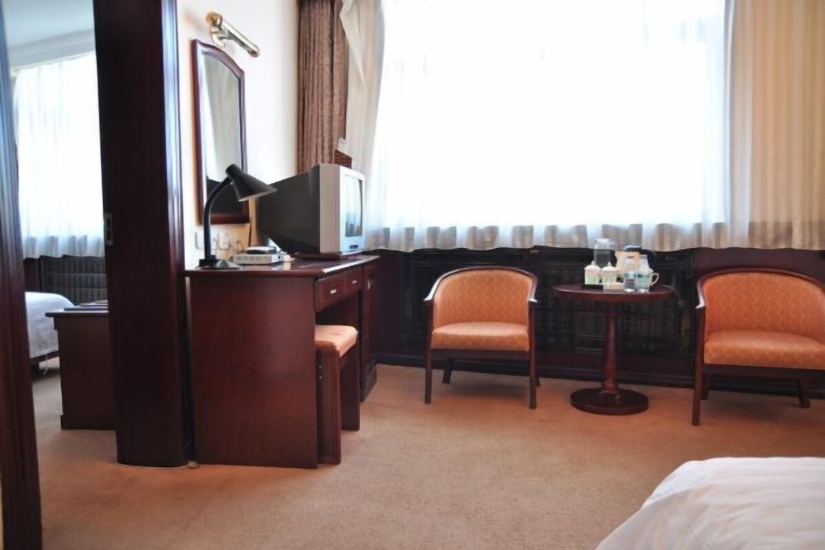 Habitación de hotel con cama, escritorio con silla, una pequeña mesa con silla y un espejo grande.