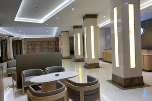 A modern hotel lobby with seating areas, a reception desk, and illuminated columns.