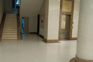 Un vestíbulo de hotel con una escalera, un mostrador de recepción y una columna.