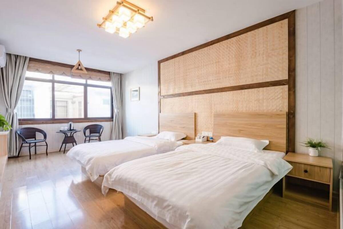 A hotel room with two beds, a wooden headboard, a small table, and a chair.