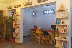 A cozy bar area with a brick counter, wooden chairs, and a bookshelf filled with books. - Qiqi Inn (Xinyang)