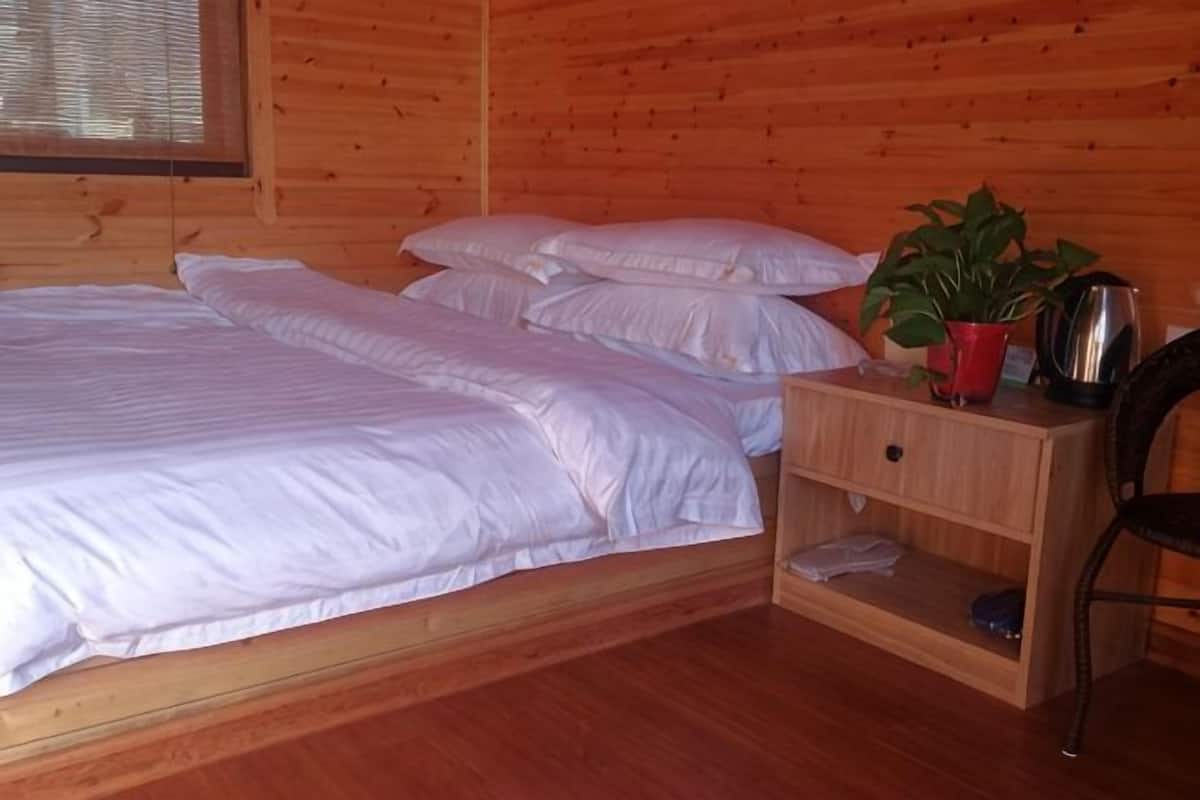A wooden cabin room with a bed, pillows, a nightstand, a plant, and a chair.