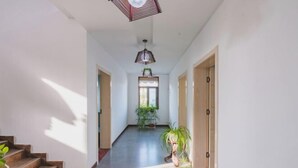 A hallway with a staircase on the left, a ceiling fan, and a window with a plant. - Qiqi Inn (Xinyang)