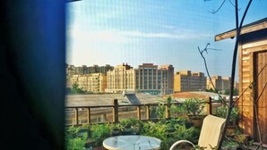 A balcony with a view of buildings, a table, chairs, and potted plants. - Qiqi Inn (Xinyang)
