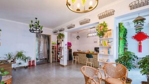 A spacious living area with wicker furniture, a bar area, and various potted plants. - Qiqi Inn (Xinyang)