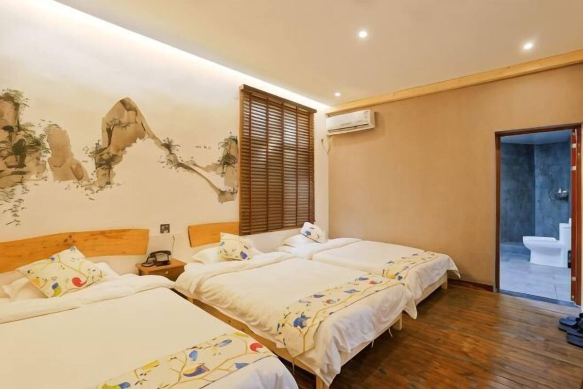 Ein Hotelzimmer mit drei Betten, Holzboden, Wandgemälde und einer Klimaanlage.