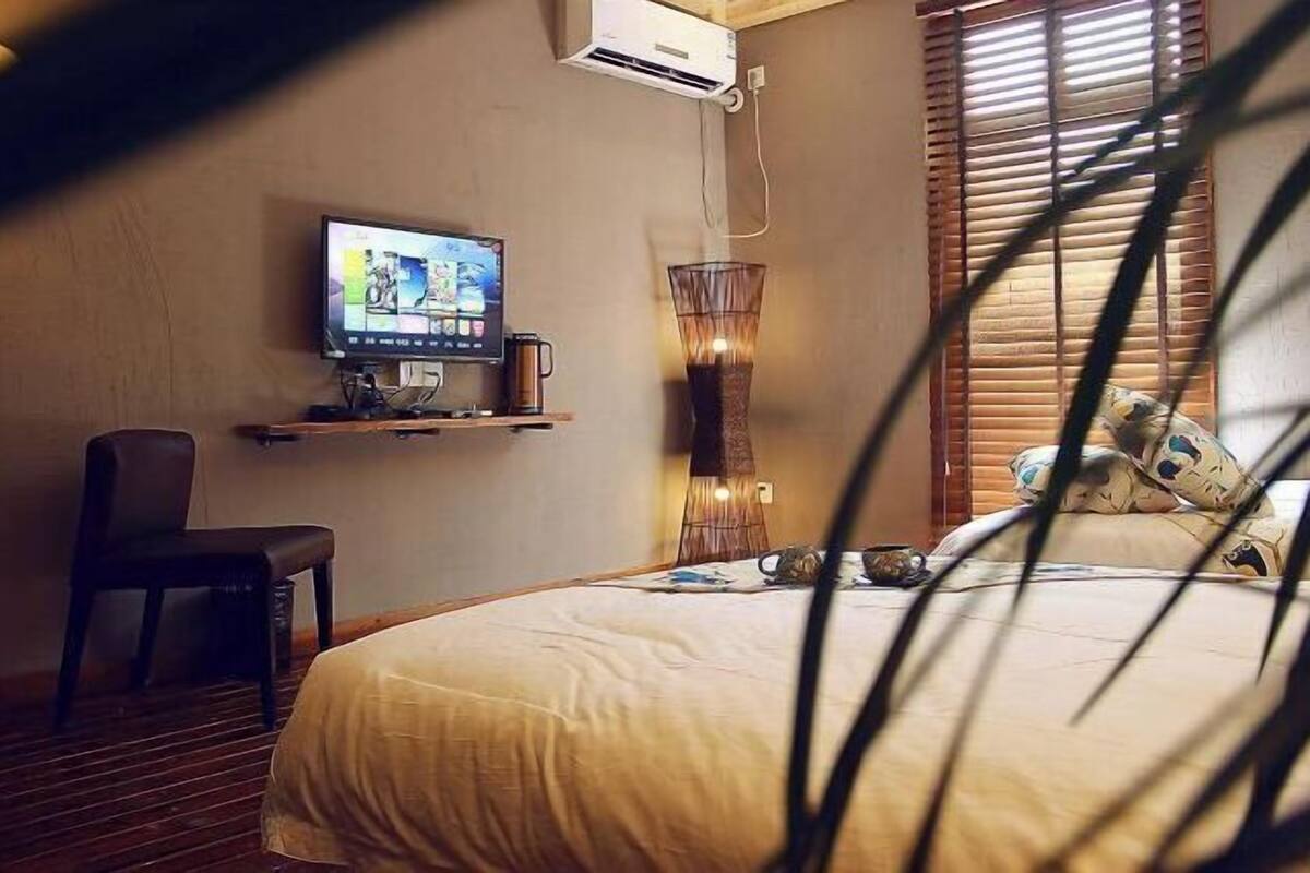 Ein Hotelzimmer mit Bett, Fernseher auf einem Tisch, einem Sessel und einem Fenster mit Jalousien.