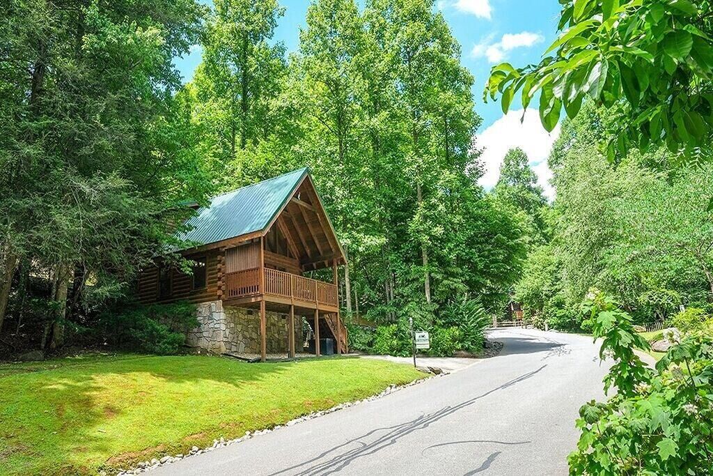A rustic cabin with a stone foundation and a wooden deck, surrounded by dense forest.
