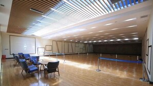 Una habitación amplia con piso de madera, una pantalla grande y sillas azules dispuestas para una reunión o presentación.