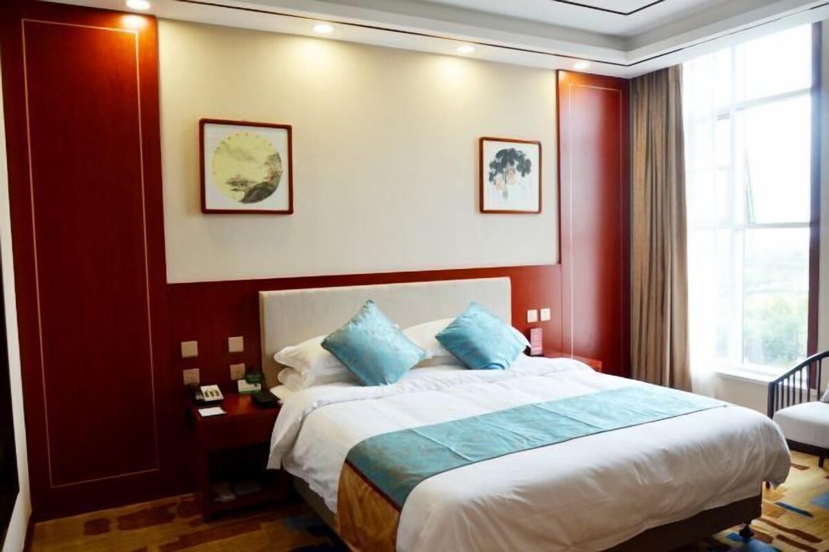 A hotel room with a large bed, two pillows, a nightstand, a desk, and a window with curtains.