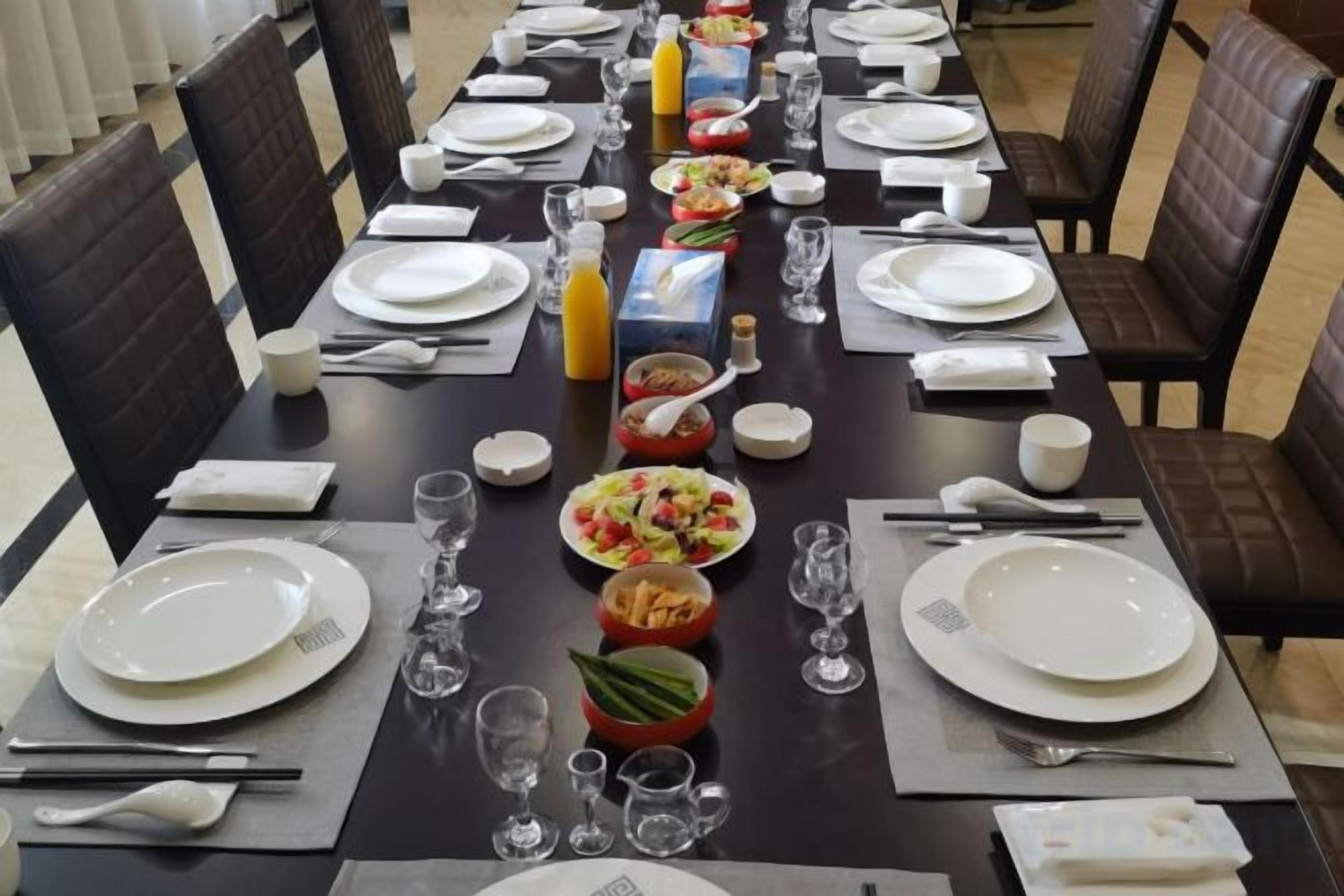 A dining table set with plates, glasses, and cutlery, surrounded by chairs.