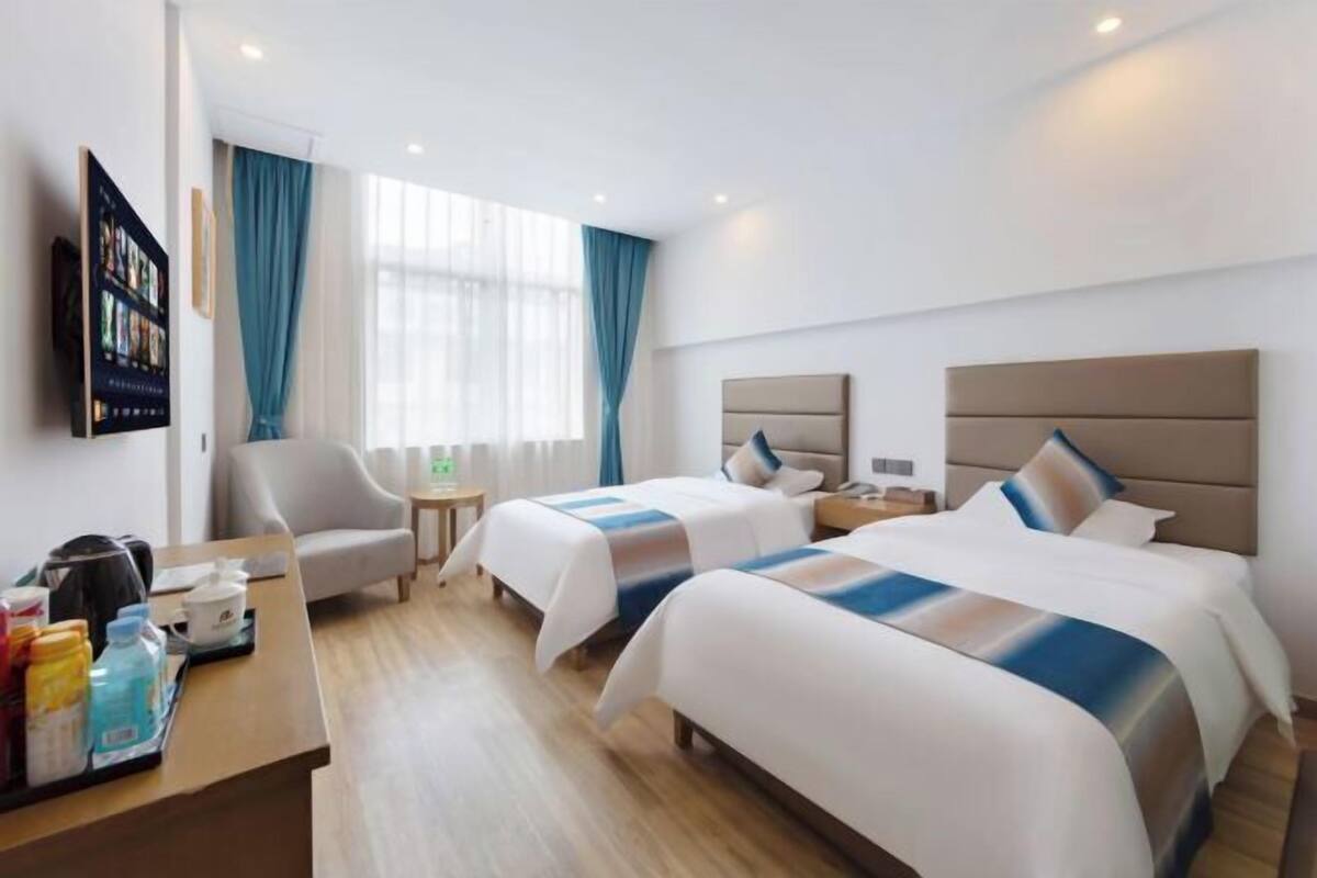 Quarto de hotel com duas camas, uma escrivaninha, uma cadeira, uma televisão e uma janela com cortinas.