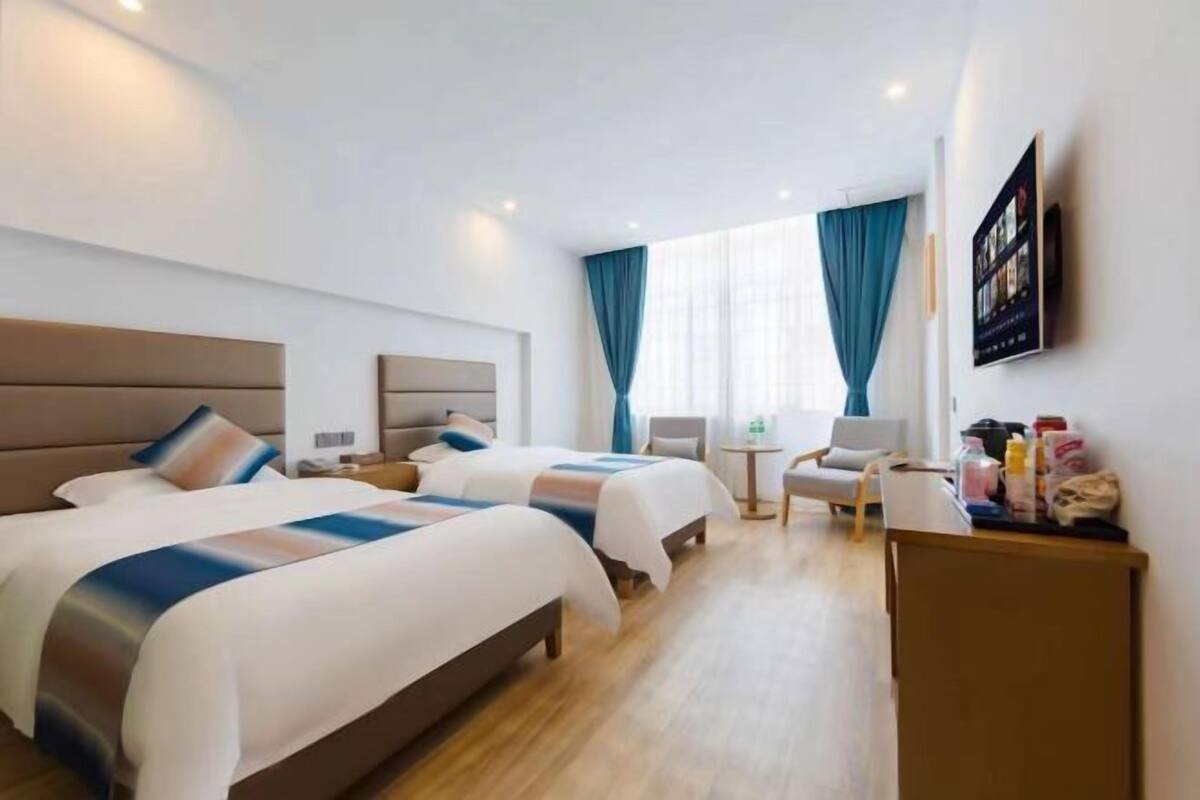 Quarto de hotel com duas camas, uma escrivaninha, uma cadeira, uma mesa pequena e uma televisão presa na parede.