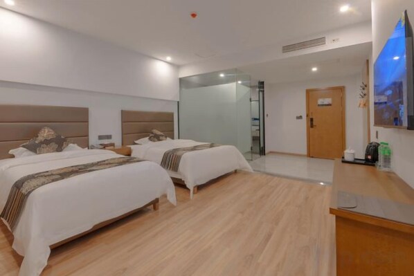 Habitación de hotel con dos camas, piso de madera, televisor de pantalla plana y mostrador de recepción.