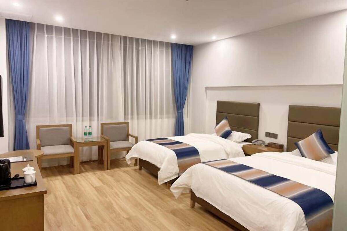 Quarto de hotel com duas camas, uma escrivaninha, cadeiras e uma mesa pequena.