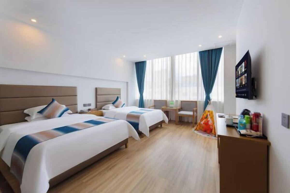 Quarto de hotel com duas camas, uma escrivaninha, uma cadeira, uma televisão e uma janela com cortinas.