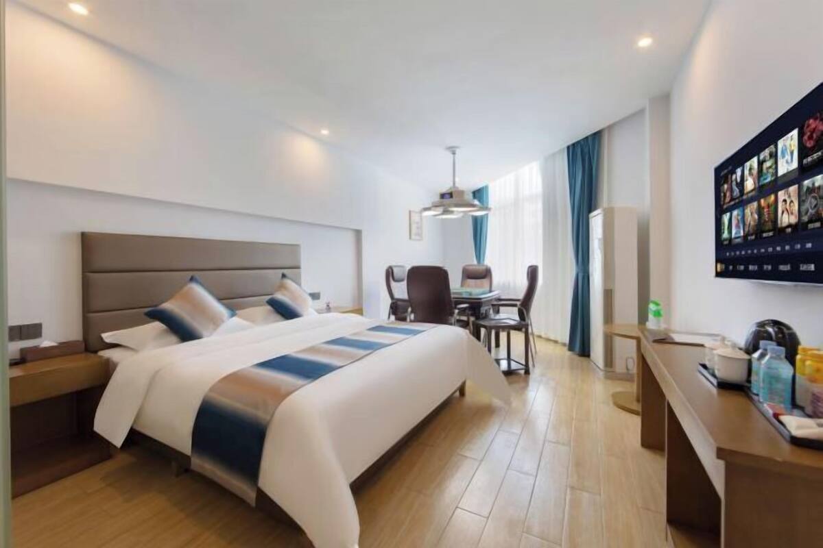 Quarto de hotel com cama, escrivaninha, cadeira, televisão e tela fixada na parede.