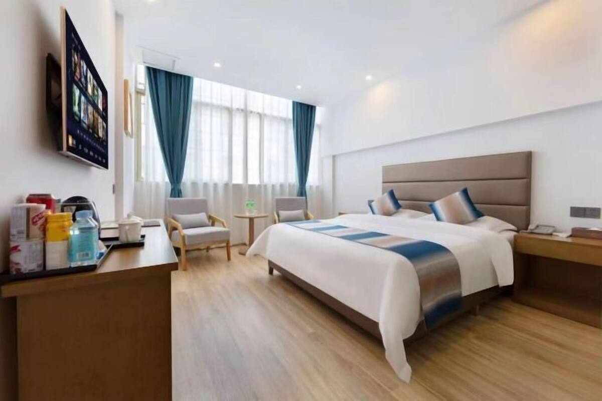 Quarto de hotel com uma cama grande, uma escrivaninha, uma cadeira e uma mesinha.