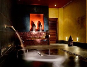 Uma área de spa com hidromassagem, uma parede decorativa com lareira e um pequeno candeeiro.