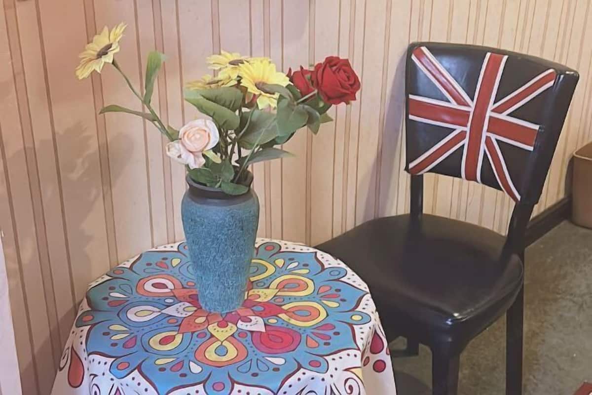Uma cadeira com estampa de Union Jack, um vaso com flores e uma mesa com padrão colorido.