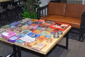 A table with various board games and books, a brown leather couch, and a plant in the background. - Not Alone Minyao Youth Hostel (Shenyang)