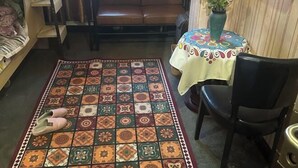 A living room with a patterned rug, a brown leather sofa, a round table with a colorful tablecloth, and a vase with flowers. - Not Alone Minyao Youth Hostel (Shenyang)