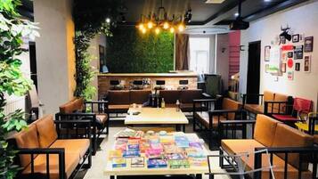 A modern cafe with multiple seating areas, a central table with magazines, and a green wall in the background.